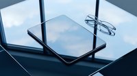 Digital tablet with glasses on a reflective glass surface near a window with sky reflection, modern workspace concept.