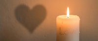 Burning candle with love inscription casting a heart-shaped shadow on a warm beige wall, evoking romance and intimacy.