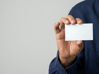 Middle-aged man with medium brown skin tone wearing dark navy shirt holding blank white business card or paper against neutral background for corporate branding.