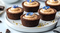 Chocolate cupcakes topped with caramel buttercream frosting, garnished with edible blue cornflowers and crushed pistachios served on white ceramic plate.