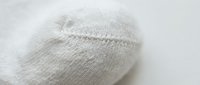 Close-up of a white cotton sock toe seam showing fine knit texture and stitching detail on a light background.