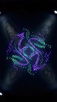 Illuminated LED light display forming geometric mandala pattern in purple and green colors on dark stage with spotlights for entertainment events.