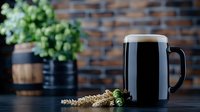 Dark craft beer in glass mug with fresh green hops and wheat ears on rustic wooden table against brick wall background. Atmospheric bar setting.