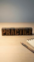 Wooden letterpress blocks spelling PRACTICE on desk with pencil and notepad for education, training, and skill development concepts.