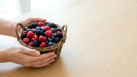 Hands holding wicker basket filled with fresh raspberries and blackberries on wooden table, organic produce and healthy eating concept.