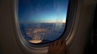 Airplane window view of illuminated city lights at dusk with aircraft wing visible, capturing twilight sky and urban landscape from high altitude for travel and aviation content.
