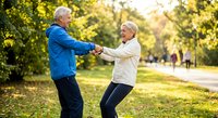 Senior couple exercising together in autumn park, holding hands while stretching outdoors for healthy active lifestyle and fitness routine.