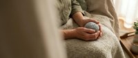 Senior woman hands holding white coffee mug while relaxing on cozy sofa at home during peaceful morning routine.