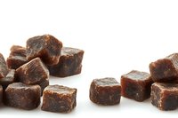 Dark brown sugar cubes scattered on white background, raw unrefined cane sugar pieces with rich caramel color and crystalline texture, isolated for food packaging design.