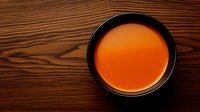 Orange-red herbal tea in black ceramic cup on dark wooden table background, top view composition for wellness and relaxation concepts.