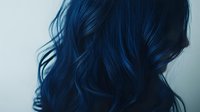 Dark blue wavy hair flowing against light background, showcasing vibrant hair dye color and soft curls in moody atmospheric lighting. Professional hair styling and coloring.