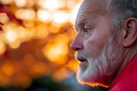 Senior Caucasian man with gray beard in profile during golden hour sunset, contemplative expression, warm lighting for lifestyle and aging concepts.