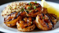 Grilled shrimp with honey glaze sauce served on white plate with rice pilaf and fresh herbs garnish, close up view of succulent seafood dinner preparation.