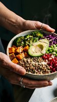 Person holding nutritious grain bowl with roasted vegetables, avocado, broccoli, sweet potato, peas and tomatoes. Healthy eating and balanced diet concept.