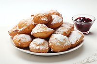 Fresh homemade donuts dusted with powdered sugar served on white plate with berry jam for breakfast or dessert treat.