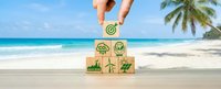 Hand placing wooden block with target symbol on pyramid of eco-friendly icons at tropical beach. Sustainable business goals and environmental strategy concept.