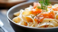 Creamy fettuccine pasta with smoked salmon, black pepper, and fresh dill garnish served in gray ceramic bowl, close up view of gourmet Italian cuisine.
