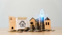 Wooden house models with stacked coins showing property investment growth and startup rocket symbol for real estate financial planning concept.