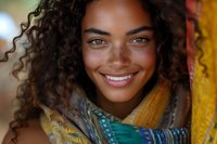 Young mixed-race woman with curly hair smiling warmly wrapped in colorful patterned scarf. Natural beauty portrait with soft lighting for lifestyle content.