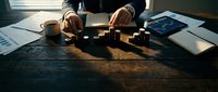 Business professional arranging wooden blocks on desk with coffee, documents and tablet in warm office lighting for strategic planning and problem solving.