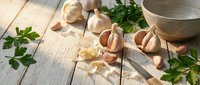 Fresh garlic bulbs and cloves with green parsley on rustic wooden table for cooking and culinary preparation.