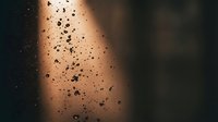Water droplets on glass surface with warm golden light creating atmospheric bokeh background for interior design and mood concepts.