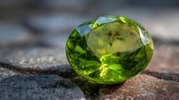 Sparkling green peridot gemstone with faceted cut on natural stone surface, showcasing vibrant color and clarity in natural sunlight.