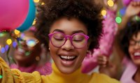 Young African American woman with natural afro hair wearing pink glasses and yellow top smiling joyfully at celebration party with colorful bokeh lights and balloons.