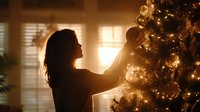 Young woman decorating Christmas tree with ornaments in warm, cozy home interior with golden holiday lights creating magical atmosphere.