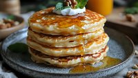 Stack of golden fluffy pancakes with syrup, whipped cream and berries on rustic plate. Delicious breakfast or brunch meal ready to serve.