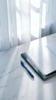 Open notebook with blue pen on marble desk by window with soft natural light creating shadows for writing and planning workspace.
