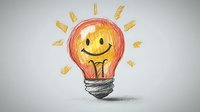 Cheerful light bulb with smiling face drawn in orange and yellow pencil colors on gray background, creative concept for innovation and bright ideas.