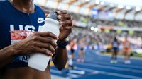 Athlete with dark skin tone holding water bottle at stadium during competition, sports hydration and fitness concept.