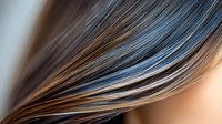Smooth flowing strands of hair in brown and blue tones create abstract waves against light background, showcasing modern hair coloring and styling techniques.