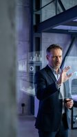 Middle-aged Caucasian male businessman in dark blazer presenting digital analytics charts and graphs on transparent holographic display in modern office environment for business technology concepts.