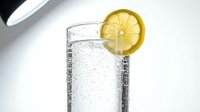 Glass of sparkling water with fresh lemon slice garnish on white background, refreshing beverage for health, wellness and lifestyle design projects.