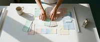 Professional woman organizing colorful sticky notes and documents on white desk for project planning and workflow management in modern office.