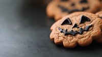 Halloween pumpkin-shaped cookies with chocolate chip jack-o-lantern faces on dark surface for autumn baking and seasonal treats.