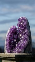 Sparkling amethyst geode cluster with deep purple crystals glittering in natural light against a soft blue sky background.