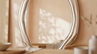 Curved glass vase with organic wavy shape on neutral beige surface, casting soft shadows, suitable for home decor and interior design projects.