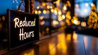 Illuminated reduced hours sign with blurred bokeh lights background, reflecting on wooden surface. Business closure concept during holiday season.