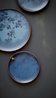 Artisanal ceramic plates with blue reactive glaze and terracotta rims arranged on dark background, showcasing handcrafted pottery for modern dining.