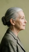 Senior woman with gray hair styled in a bun, wearing a taupe blazer, shown in profile against a neutral background. Suitable for healthcare, wellness, and lifestyle editorial use.