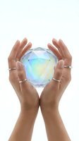 Hands holding iridescent crystal sphere with rainbow light reflections on white background, isolated for design use and spiritual concepts.