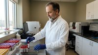 Middle-aged Caucasian male scientist in white lab coat working with test tubes in modern laboratory setting for medical research and healthcare studies.