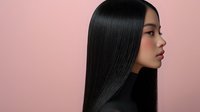 Asian woman with sleek, straight black hair in profile against pink background, showcasing healthy, shiny hair for beauty and haircare advertising.
