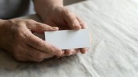 Adult male hands holding blank white business card on neutral linen fabric background for corporate branding and professional networking purposes.
