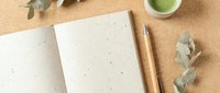 Open notebook with blank pages, wooden pencil, and eucalyptus leaves on cork surface. Flat lay composition for stationery, writing, planning, and creative projects.