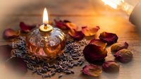 Romantic candle burning in decorative glass holder surrounded by dried rose petals and coffee beans creating warm intimate atmosphere for spa relaxation.