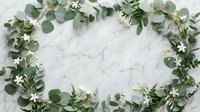 Fresh eucalyptus branches with small white flowers arranged in decorative frame border on white marble background for wedding invitations and botanical designs.